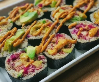 A savory vegan sushi bake with layers of rice, tofu, avocado, and nori, topped with spicy mayo.